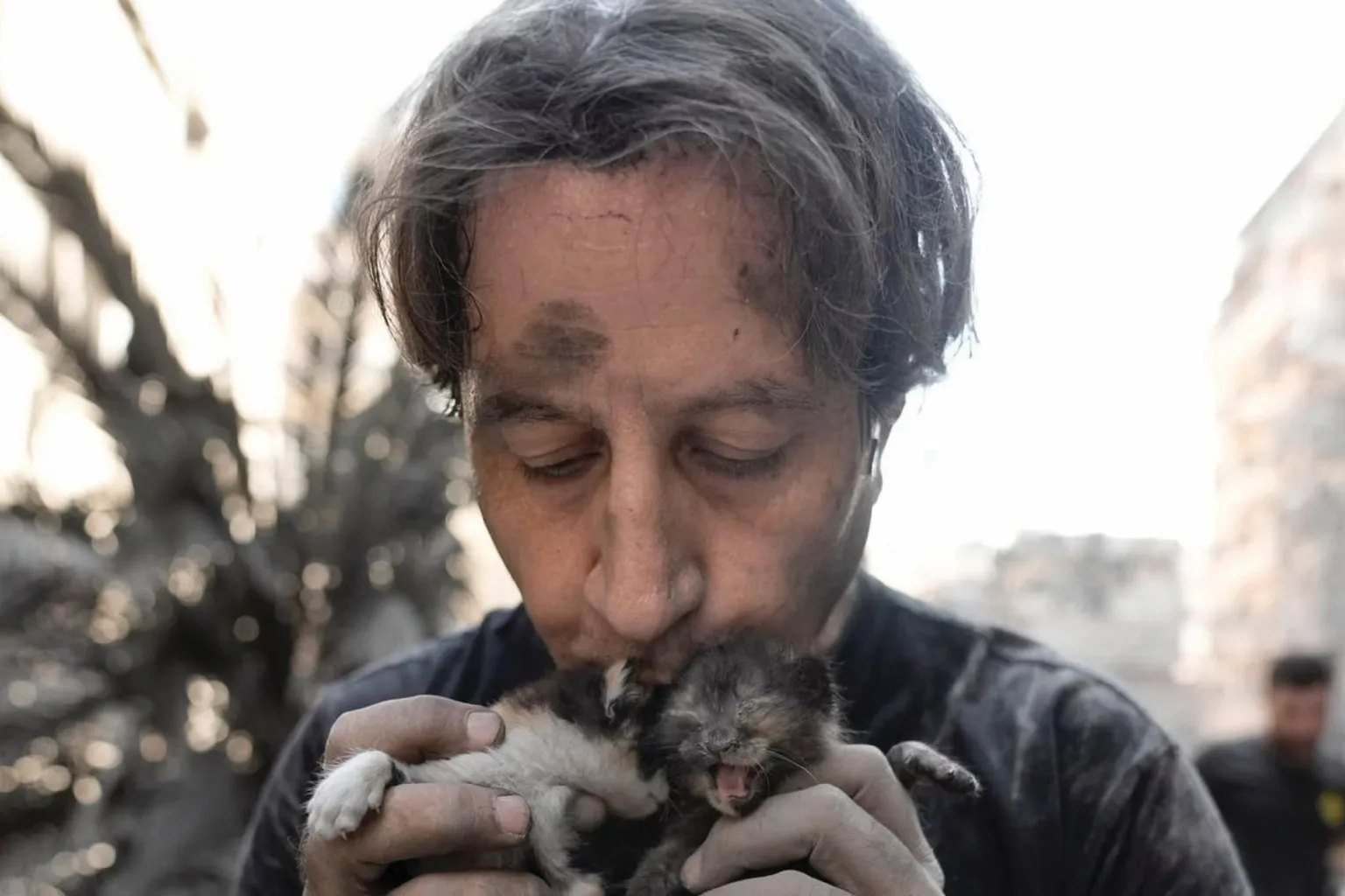 An Animals Lebanon rescuer, his face streaked with dust, kissing a newborn kitten he is holding